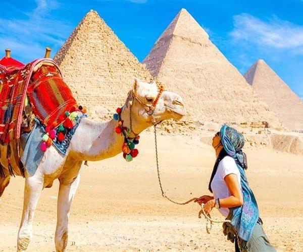 Woman interacting with camel near pyramids