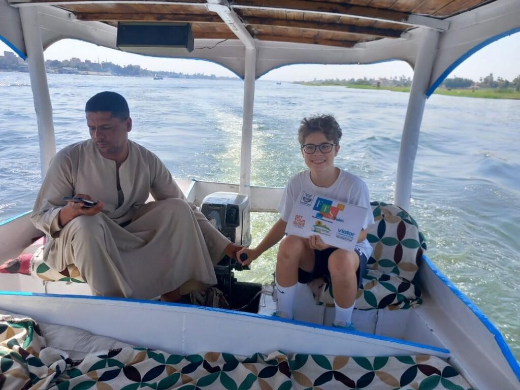 A boy with glasses holding a tour sign on a boat.